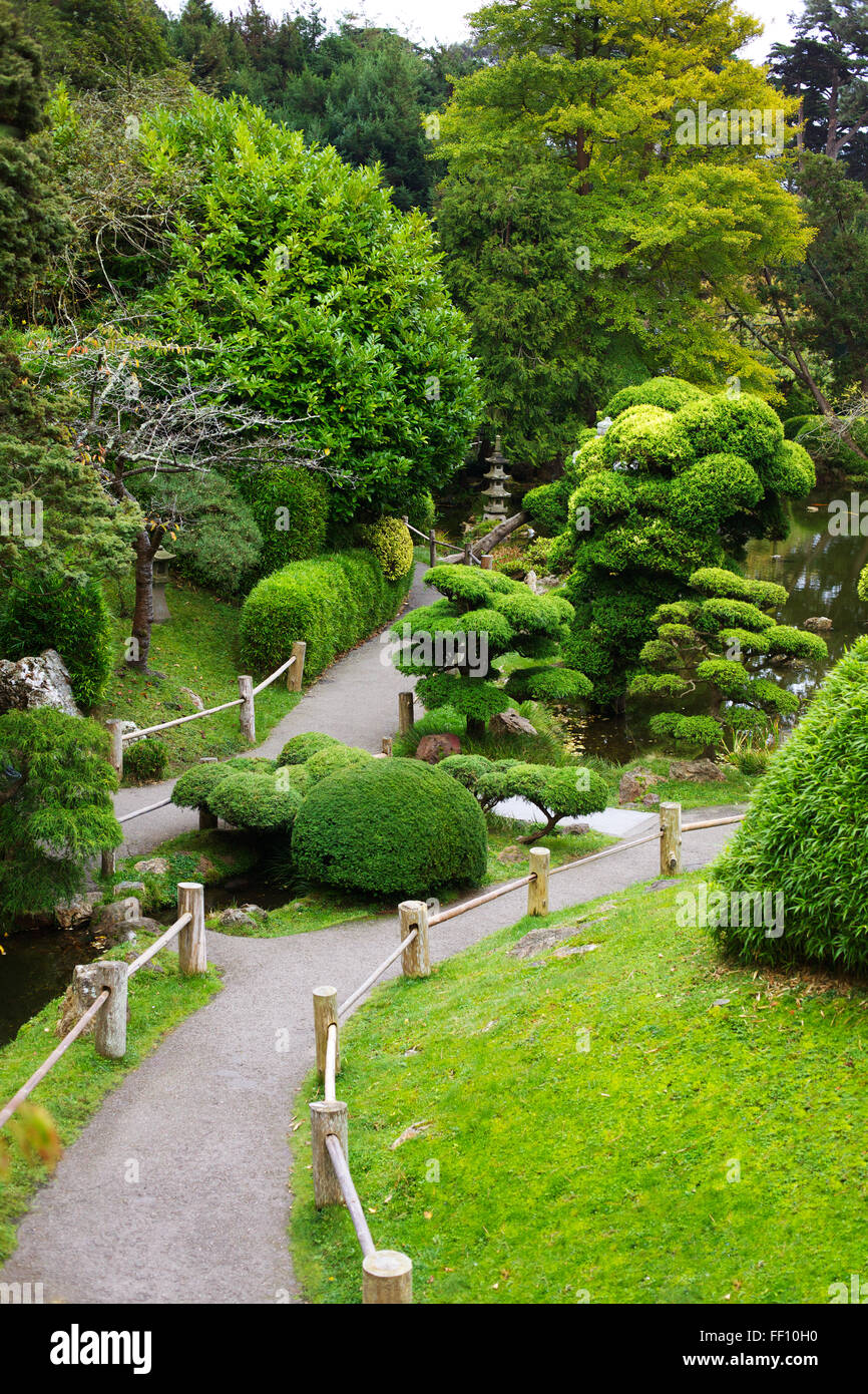 A pathway winding though a Japanese garden, the bushes, trees and grass are all vibrant green. Stock Photo