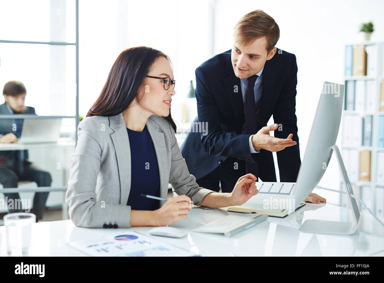 Pretty secretary discussing ideas with colleague in front of computer ...