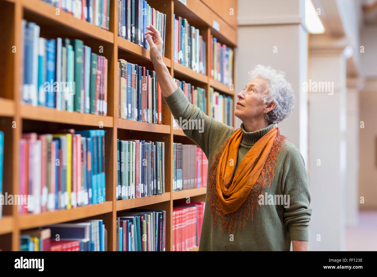 Older mixed race woman choosing book in library Stock Photo