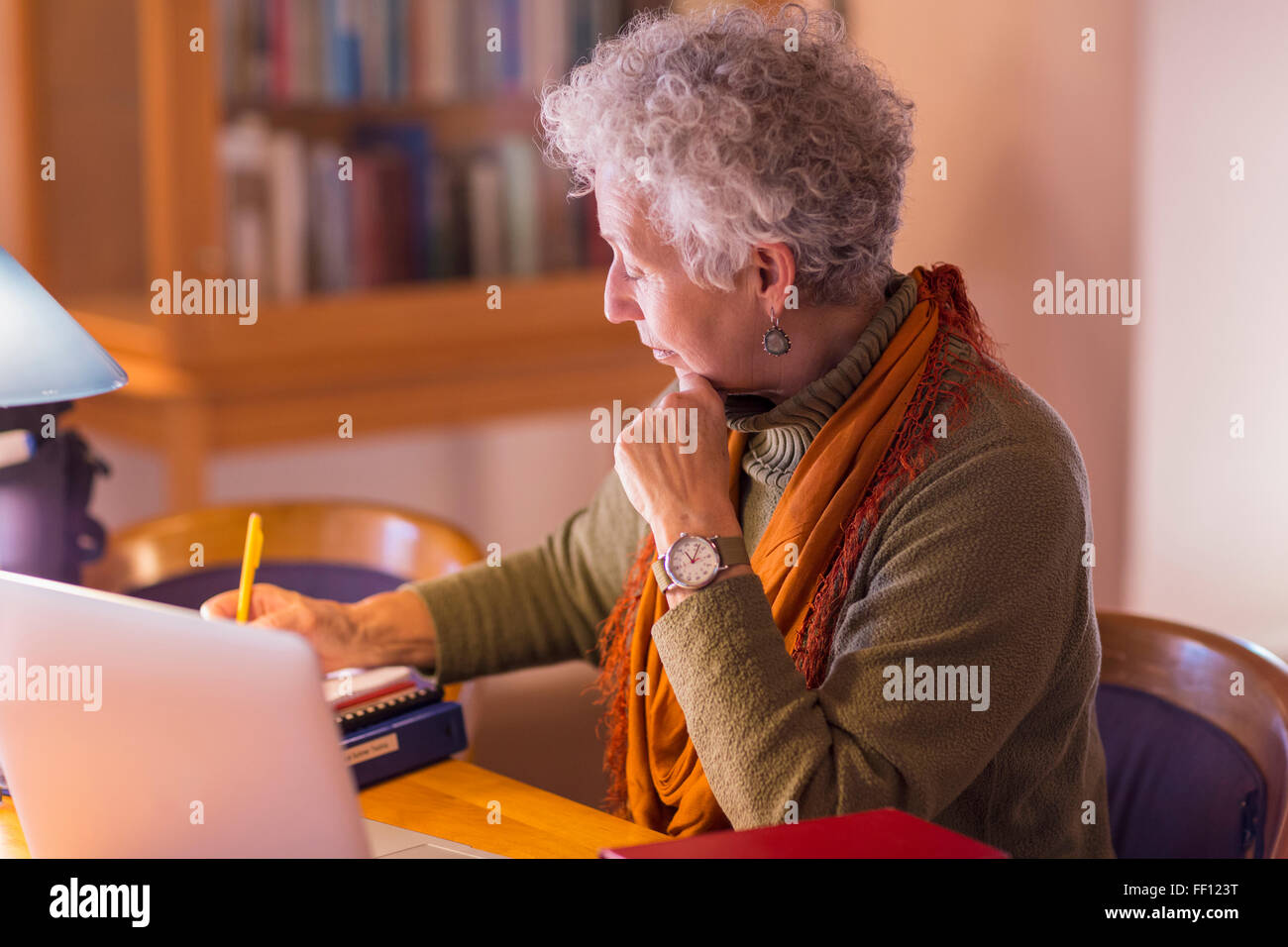 Older mixed race woman writing in library Stock Photo