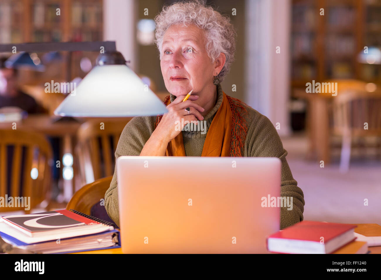 Older mixed race woman using laptop in library Stock Photo
