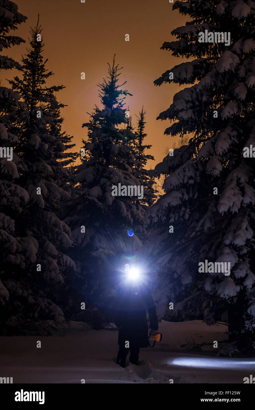Caucasian hiker wearing headlamp in snowy forest Stock Photo