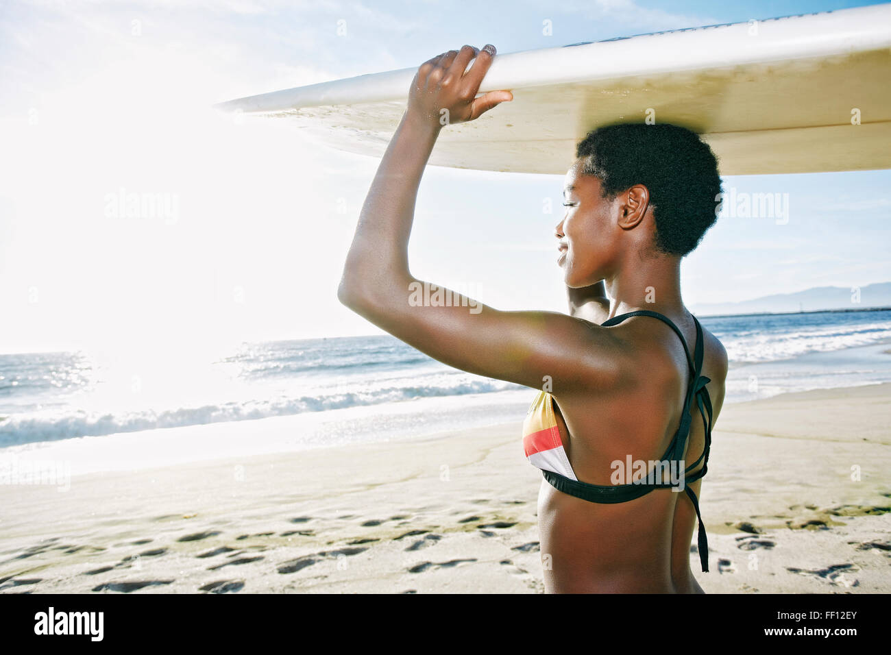 Black woman balancing surfboard on head at beach Stock Photo
