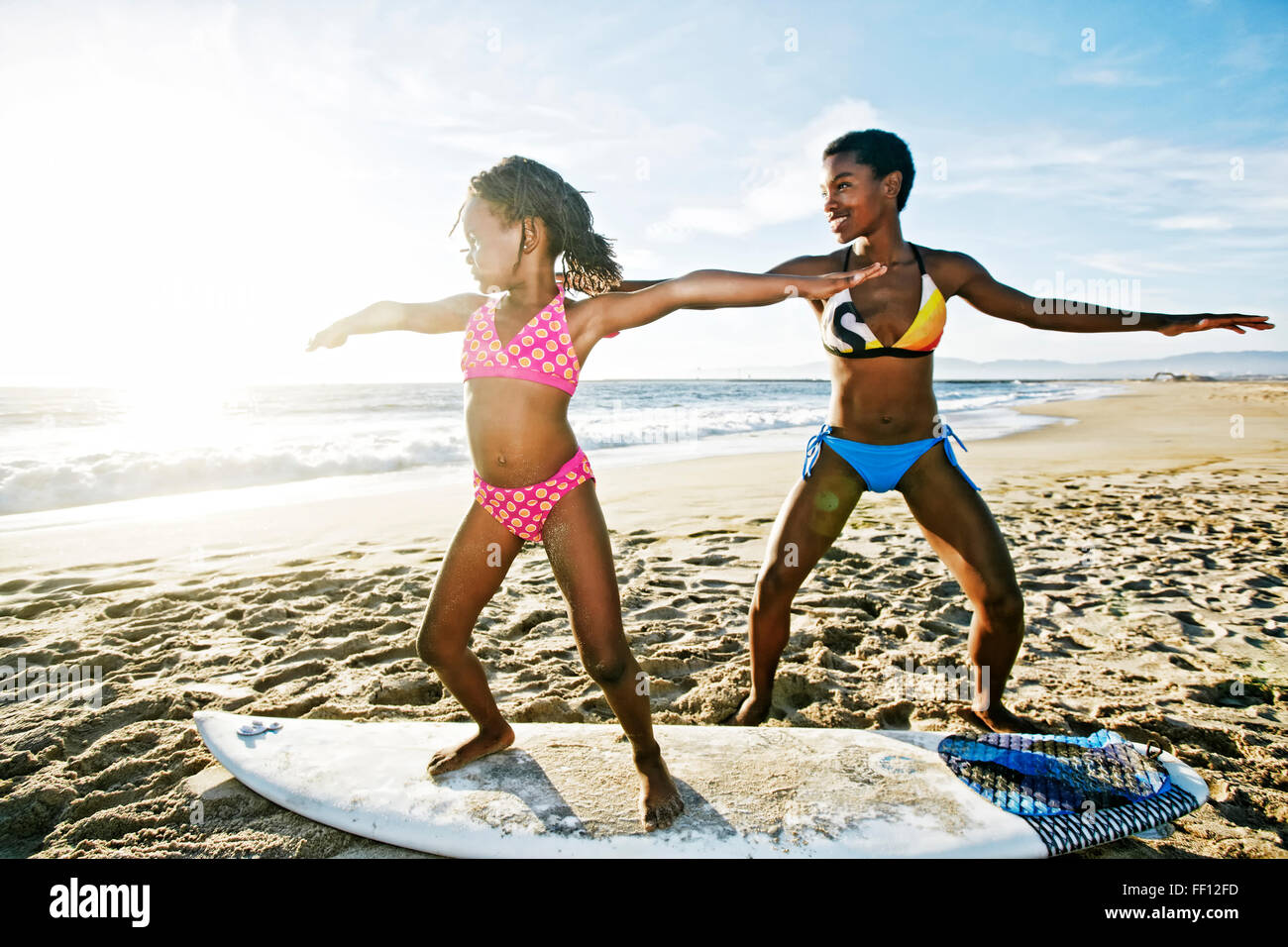 Black mother teaching daughter to surf on beach Stock Photo