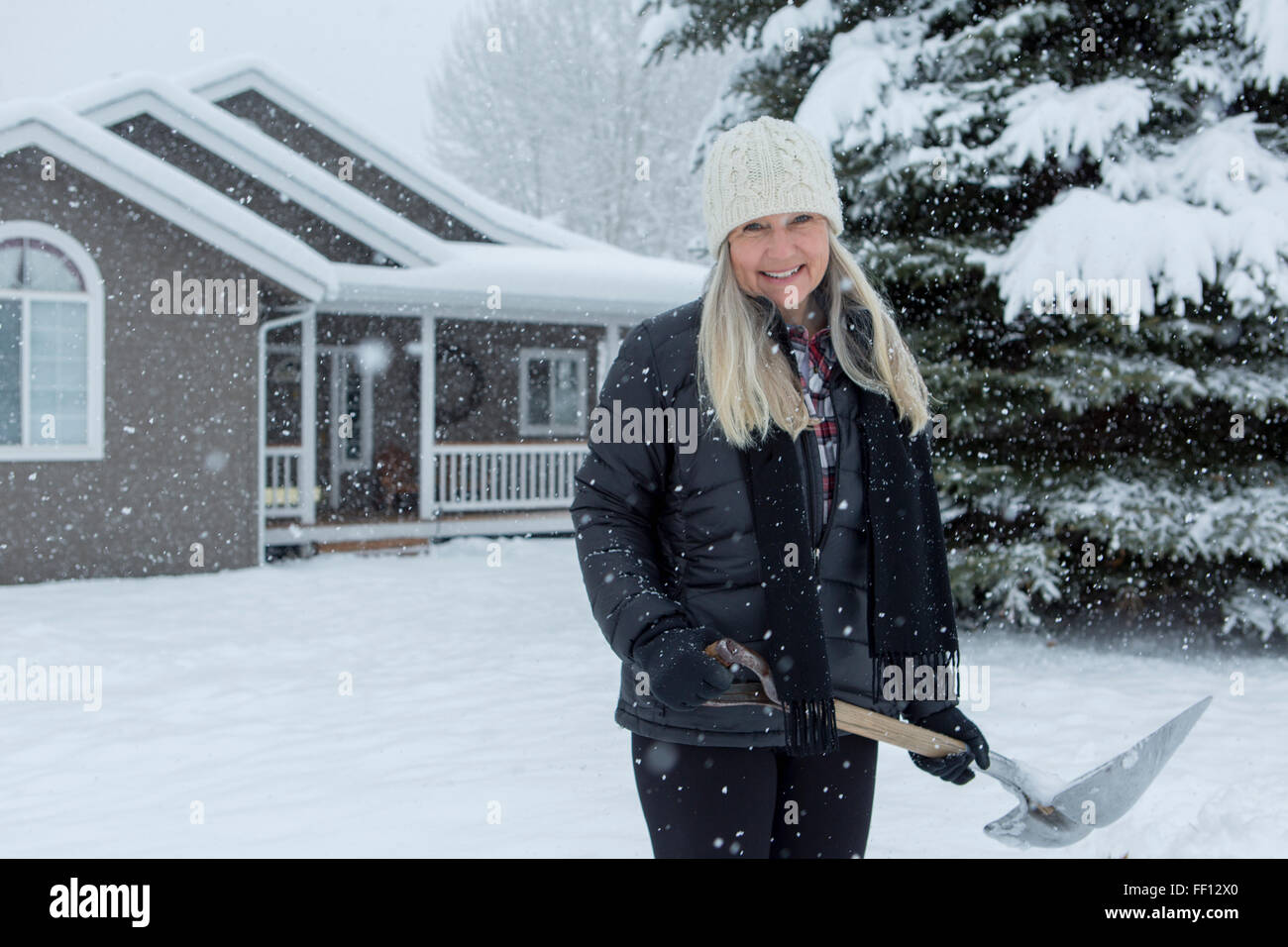 Older Caucasian woman shoveling snow in front yard Stock Photo