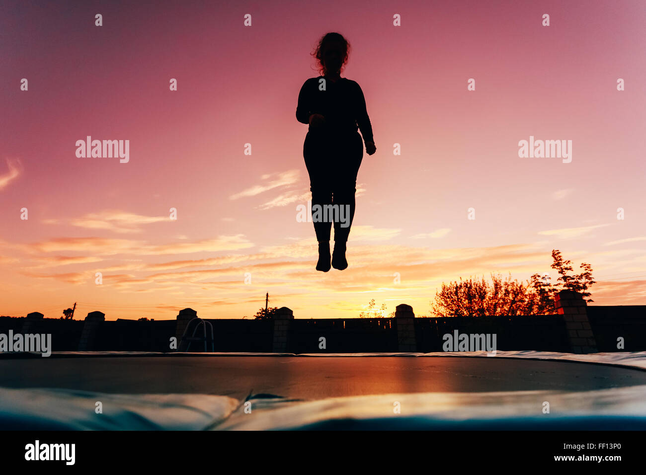 Silhouette Of Beautiful Plus Size Young Woman Girl Jumping On Trampoline On Evening Blue Sky Background Stock Photo