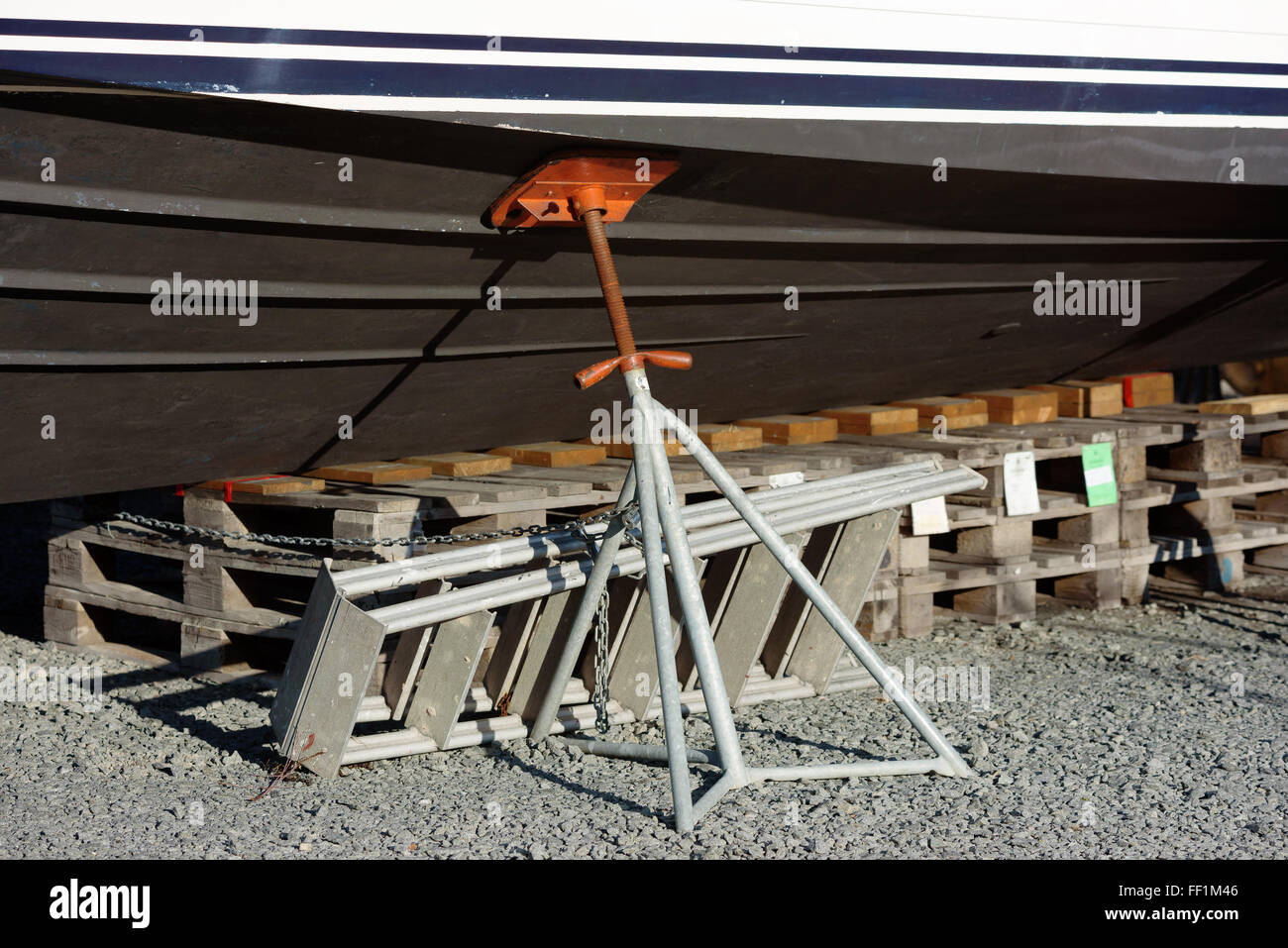 An adjustable, tilting metal boat stand support the keel from the side. The underside of the keel rests on pallets. Chain and pa Stock Photo