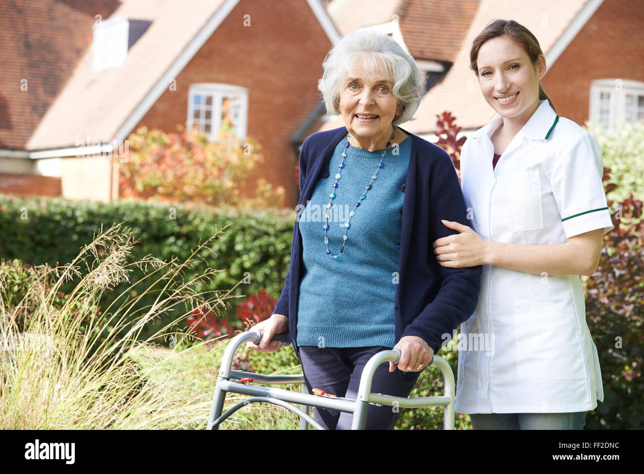 Carer Helping Senior Woman To Walk In Garden Using Walking Frame Stock Photo