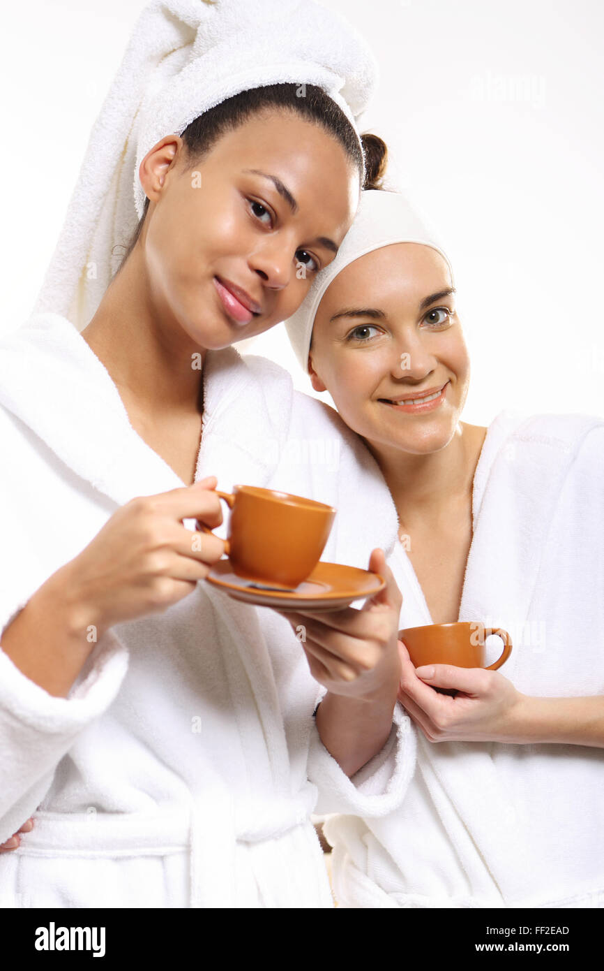 Two women in wellness salon dressed in white robes with cups of coffee