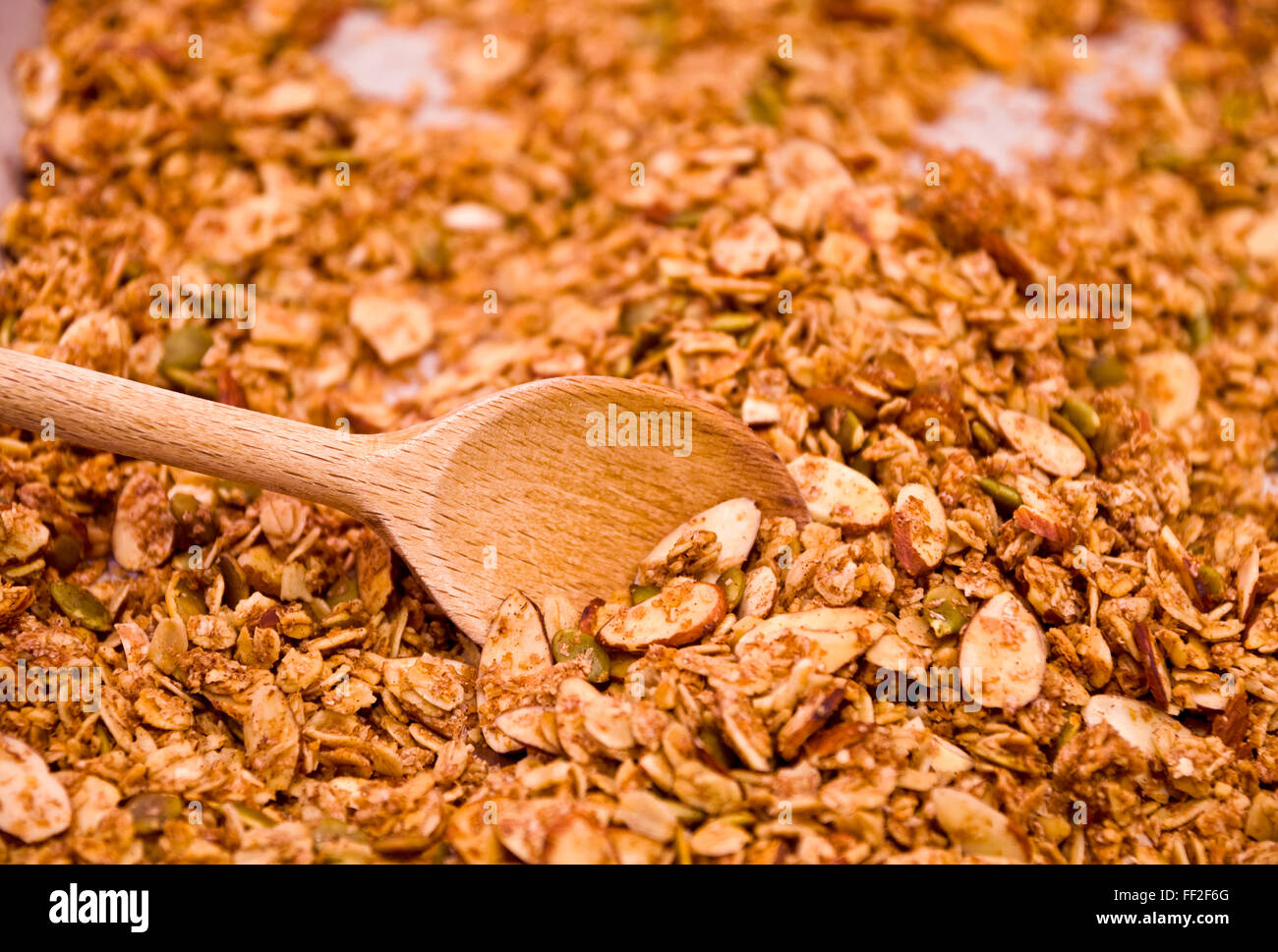 Stirring cookie sheet of homemade granola with wooden spoon. Stock Photo