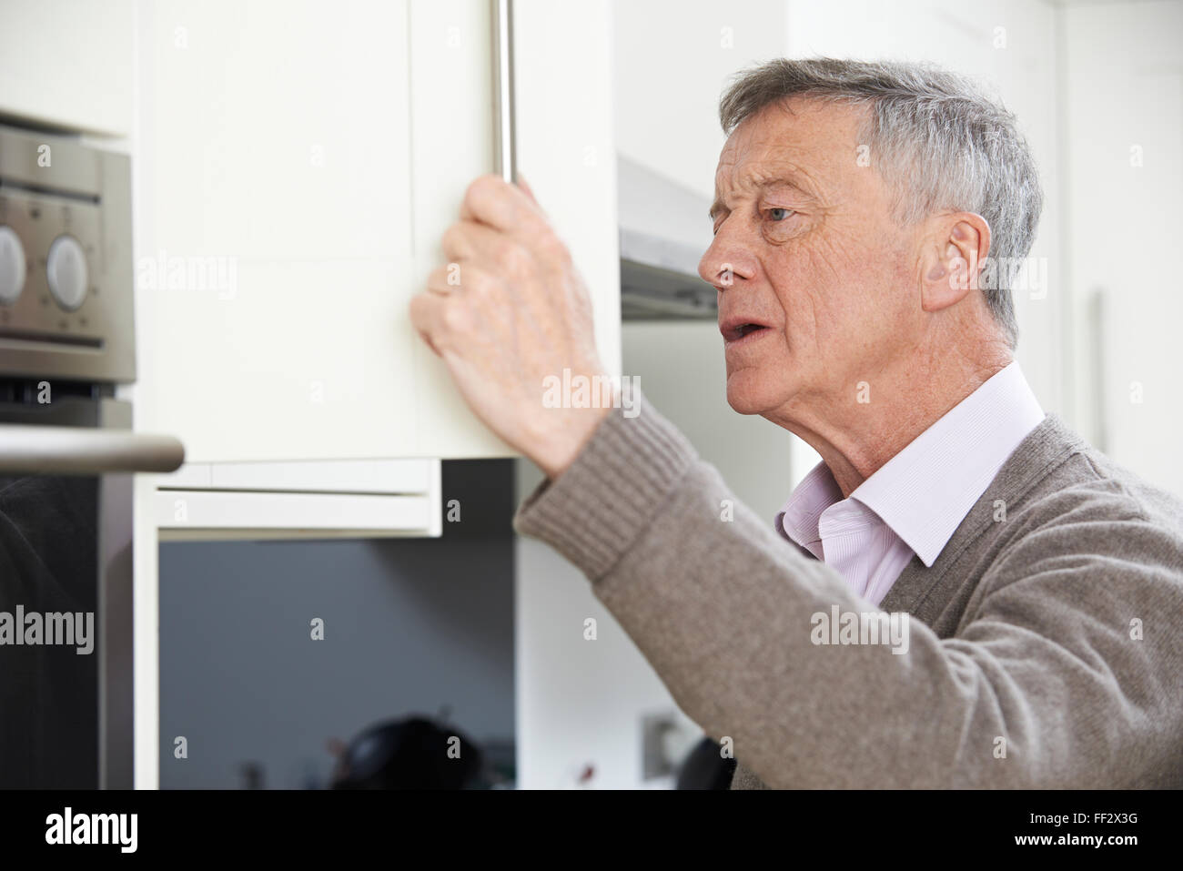 Forgetful Senior Man Looking In Cupboard Stock Photo