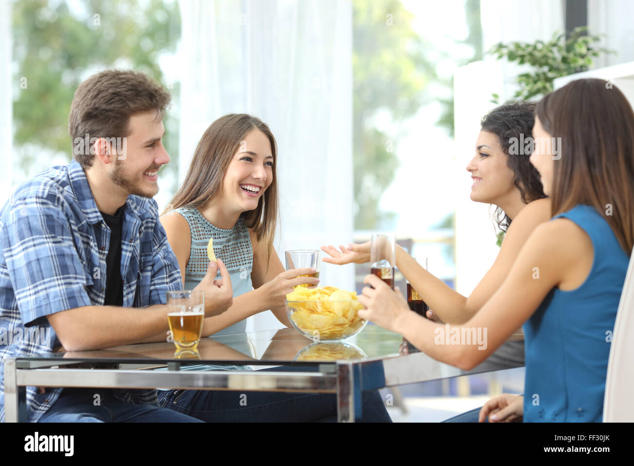 Funny group of 4 friends having a conversation and drinking at home Stock Photo