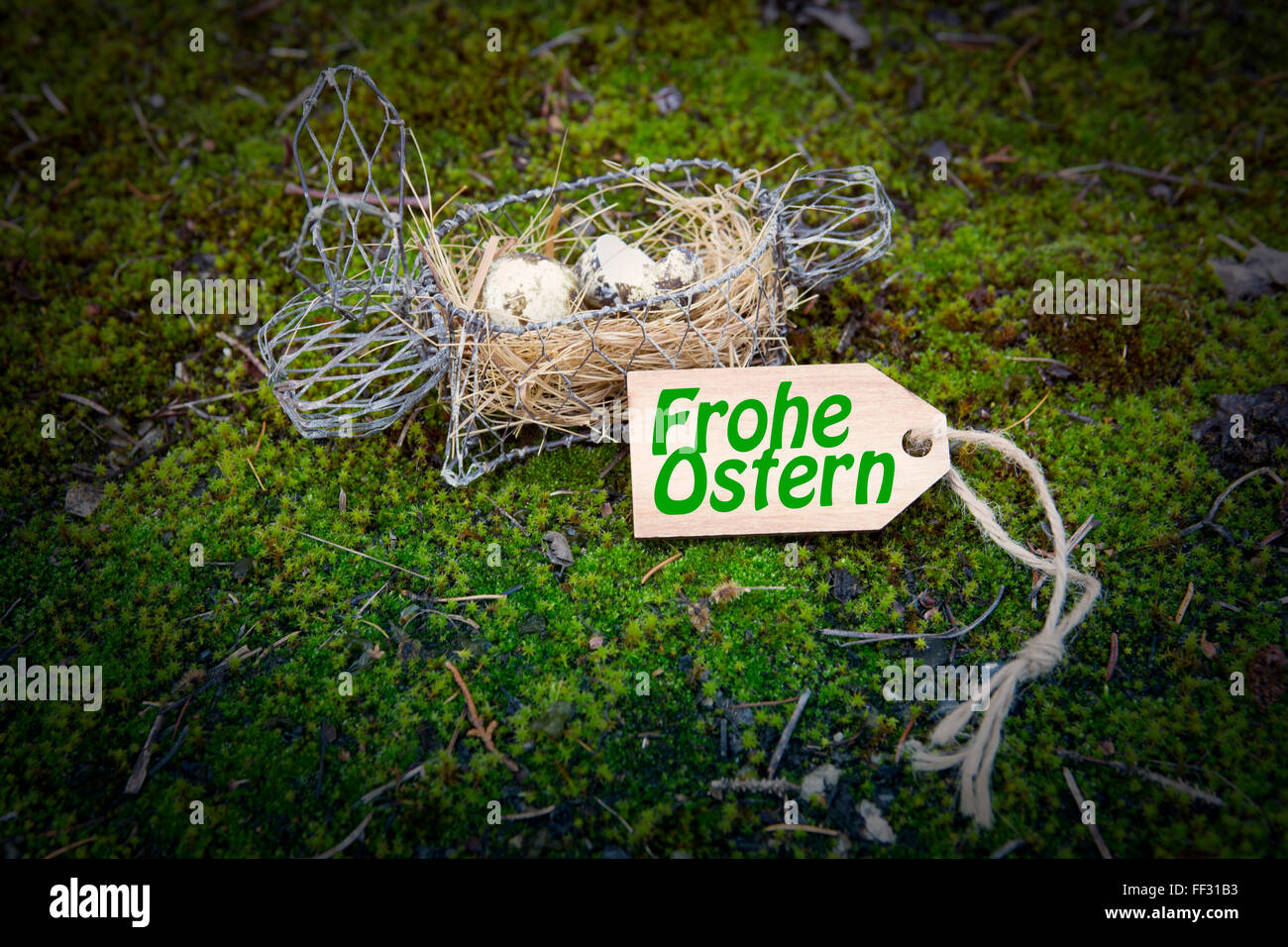 german 'Frohe Ostern' (Happy Easter) on wooden tag with easter bunny basket on green moss Stock Photo