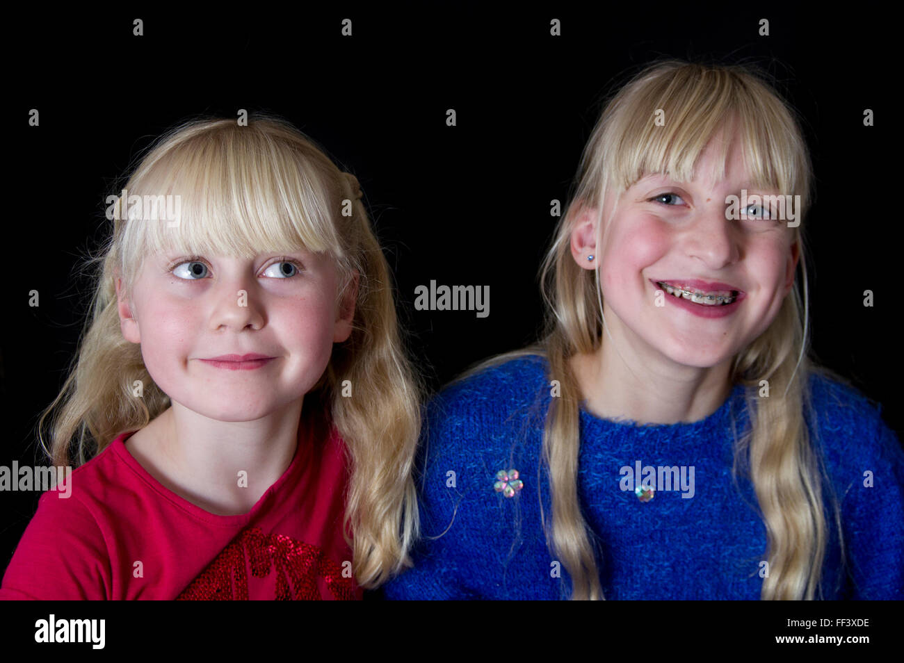 Studio portrait of two young, blond girls against a black background. Stock Photo