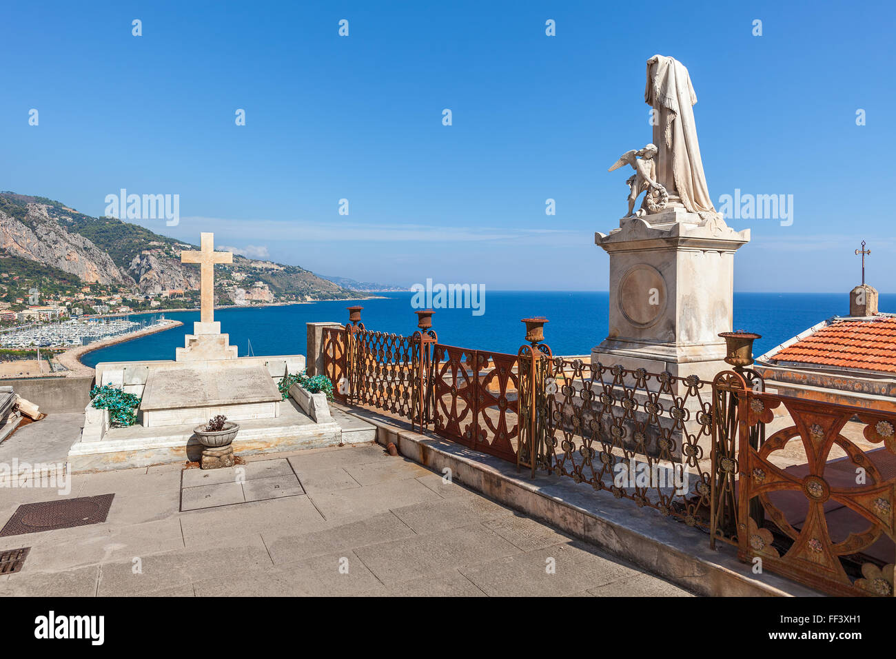 Statue and tomb with cross at old cemetery with view on Mediterranean sea in Menton, France. Stock Photo