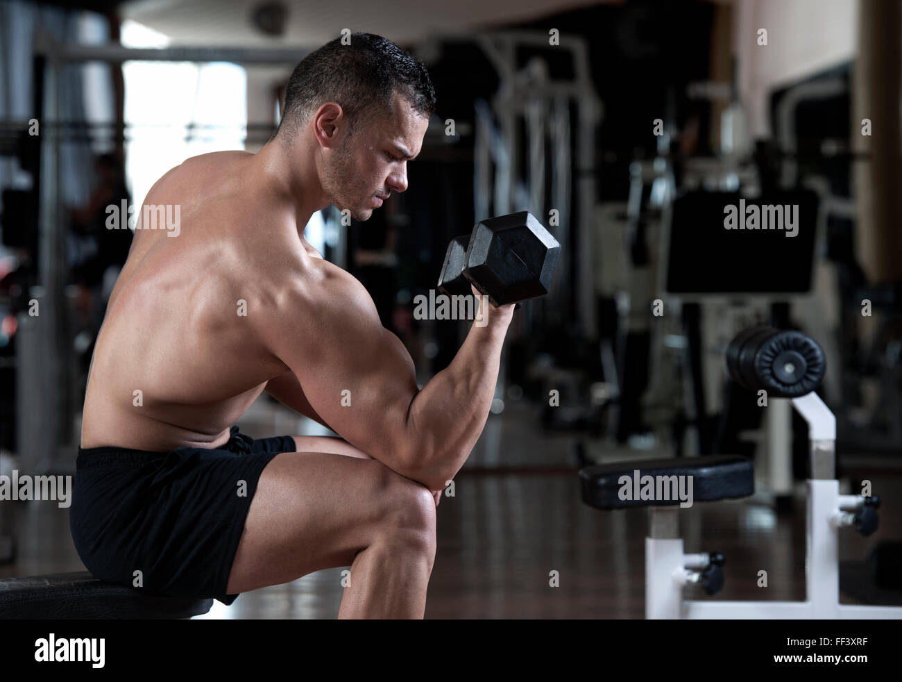 very power athletic guy bodybuilder execute exercise with dumbbells in dark gym Stock Photo