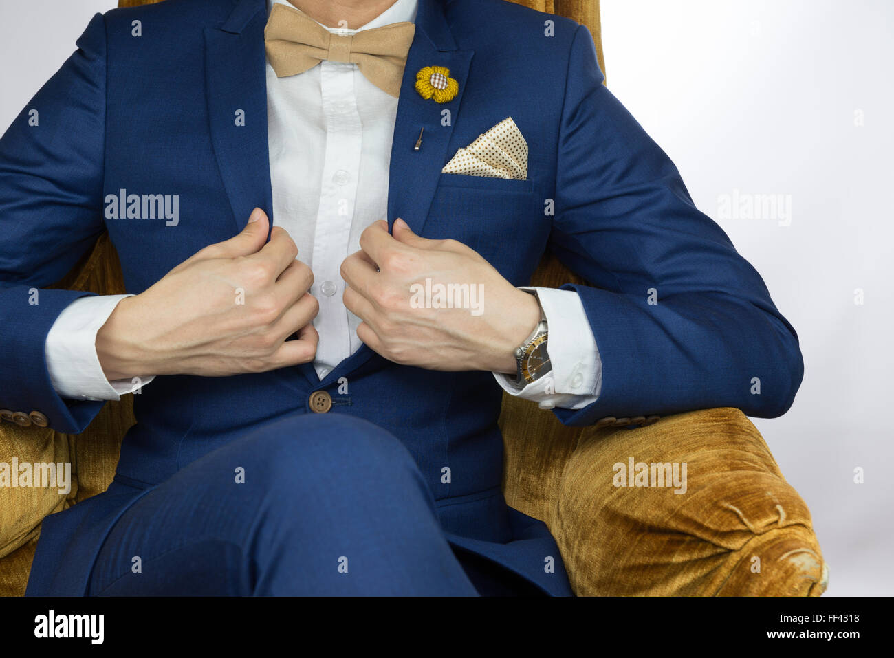 Man in blue suit with coffee cream bowtie color, flower brooch, and dot pattern pocket square sitting on cozy sofa Stock Photo