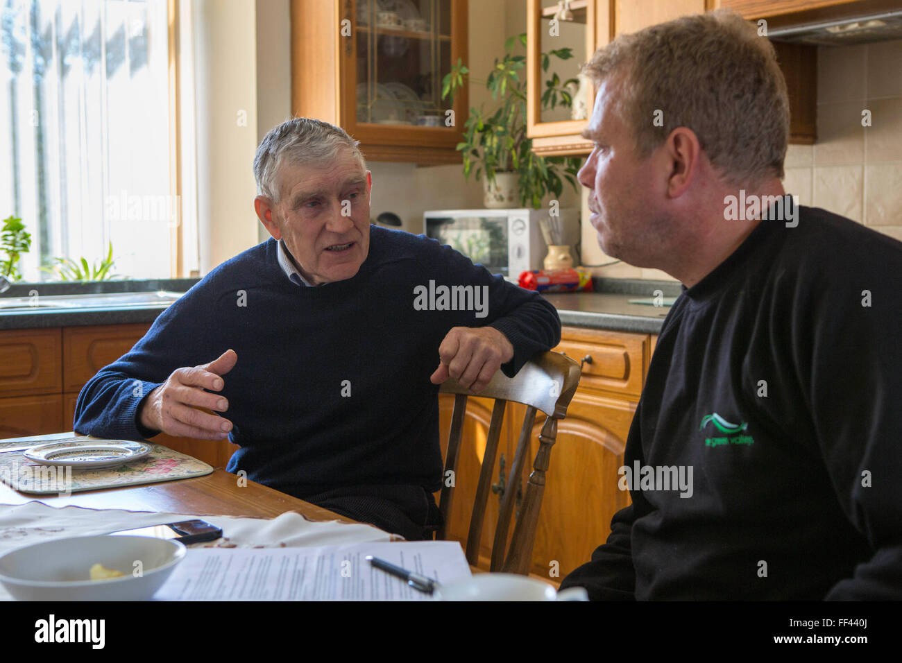Farmer Howell Williams and Chris Blake of The Green Valleys  sitting in the farm kitchen discussing the 15kW micro hydro power generator producing electricity at Abercrave Farm on the Brecon Beacons, Wales. Stock Photo