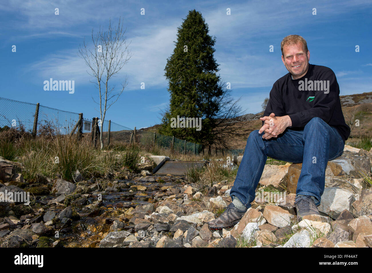 Chris Blake of The Green Valleys sitting by the entry point to the Abercrave Farm 15kW hydro power plant on the Brecon Beacons, Wales. Stock Photo
