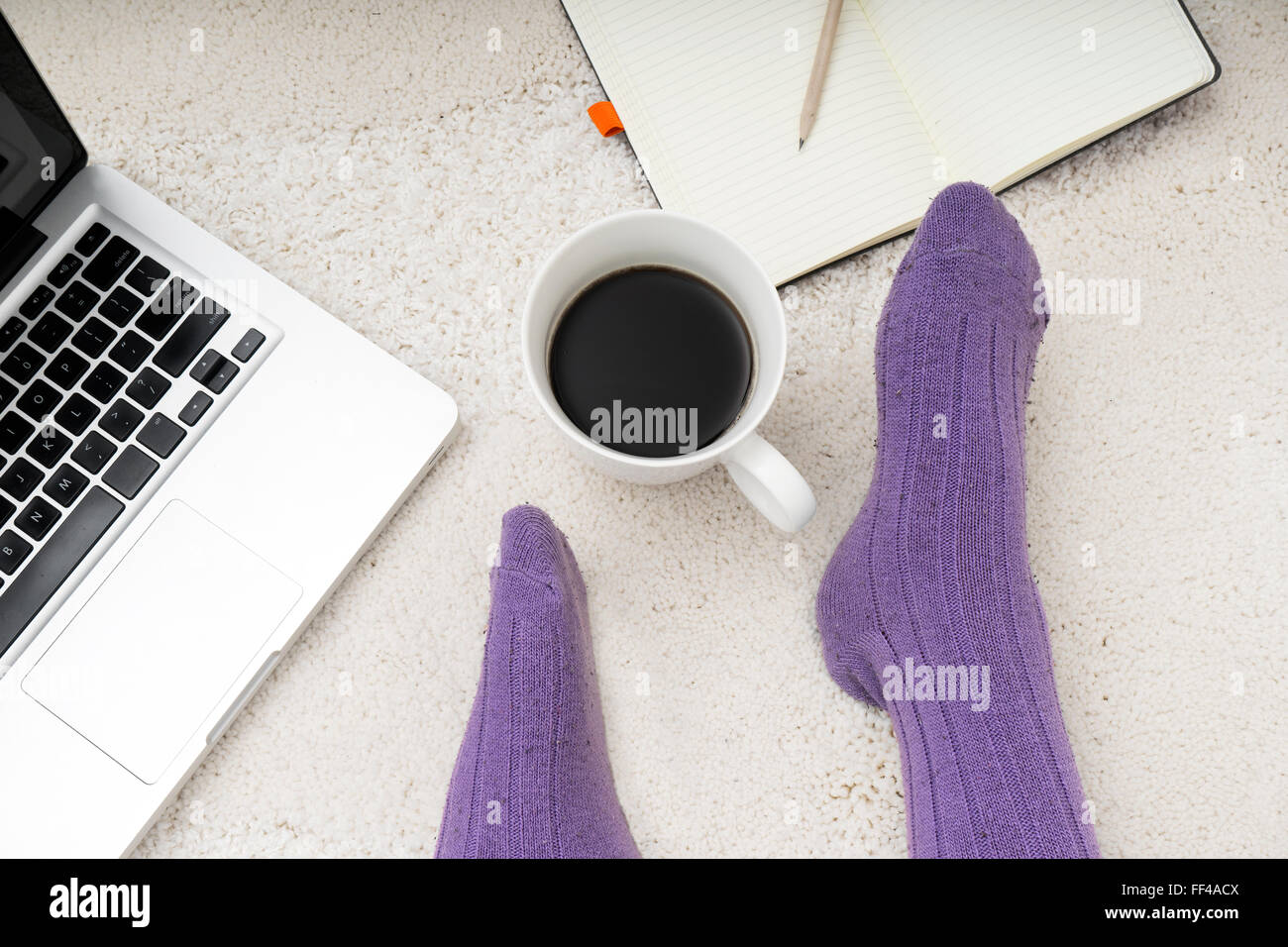 Overhead shot of woman feet, laptop, coffee and notebook on the white carpet Stock Photo