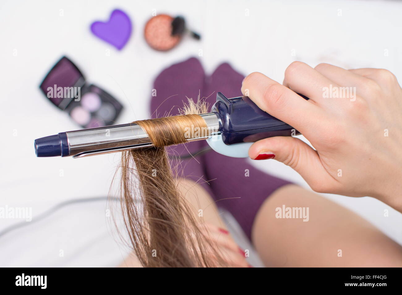 Top view of a girl straightening her hair while sitting in bed Stock Photo
