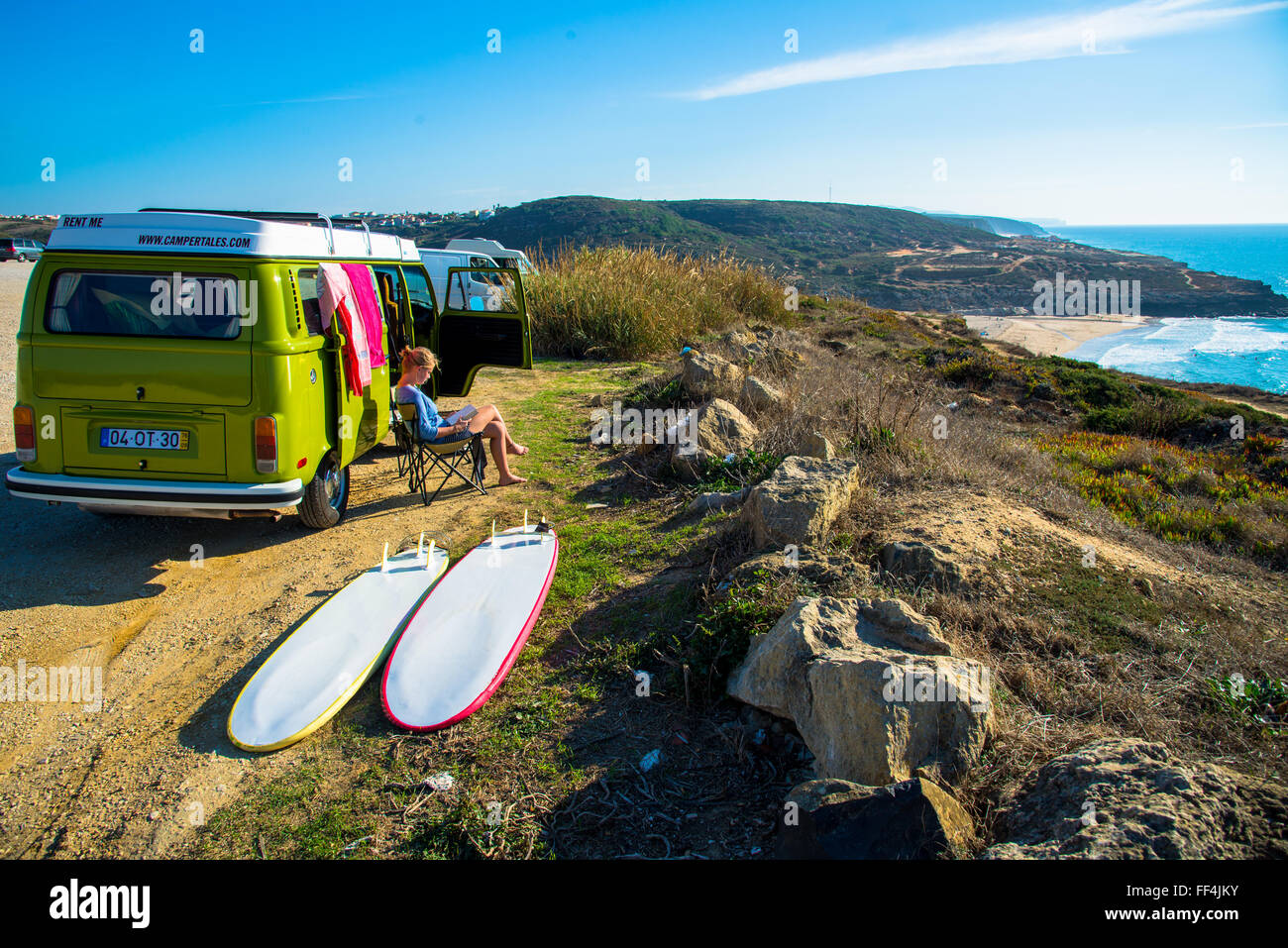 girl sitting next to camper with surfboards at coast of portugal near ericiera Stock Photo