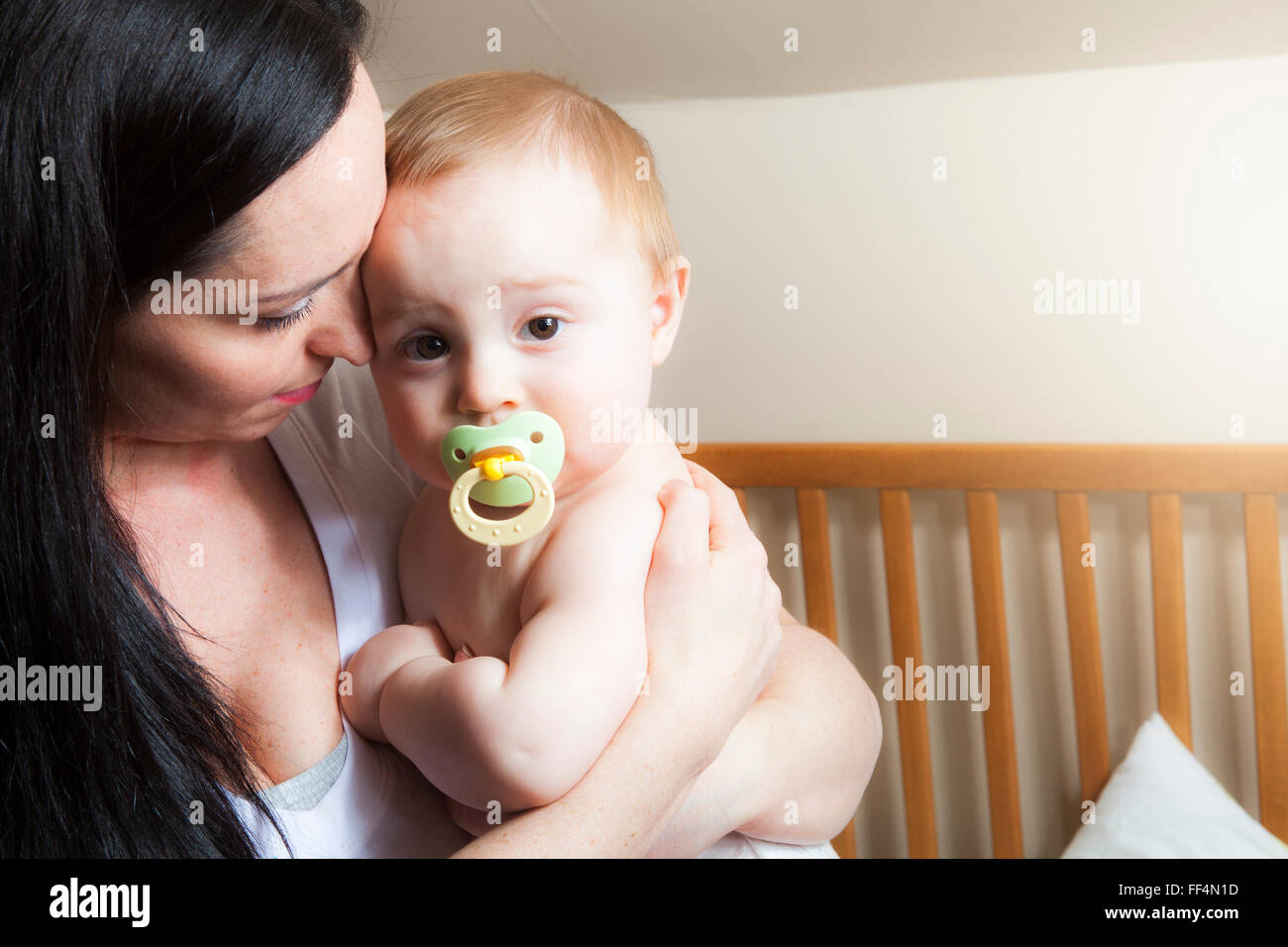 Devoted mother laying son down into crib for nap in bedroom Stock Photo
