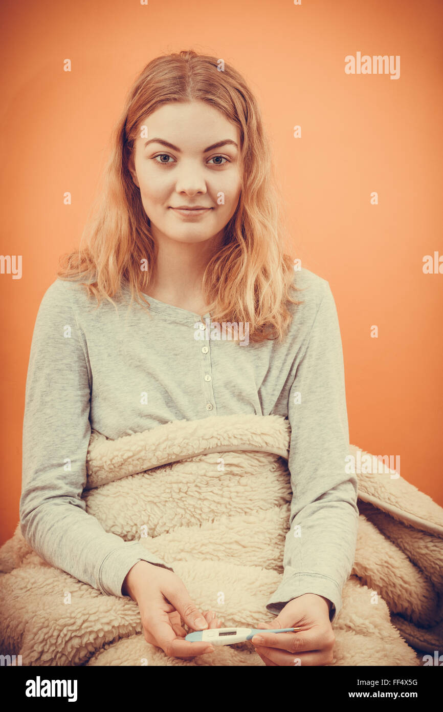Sick ill woman under blanket with digital thermometer. Young girl