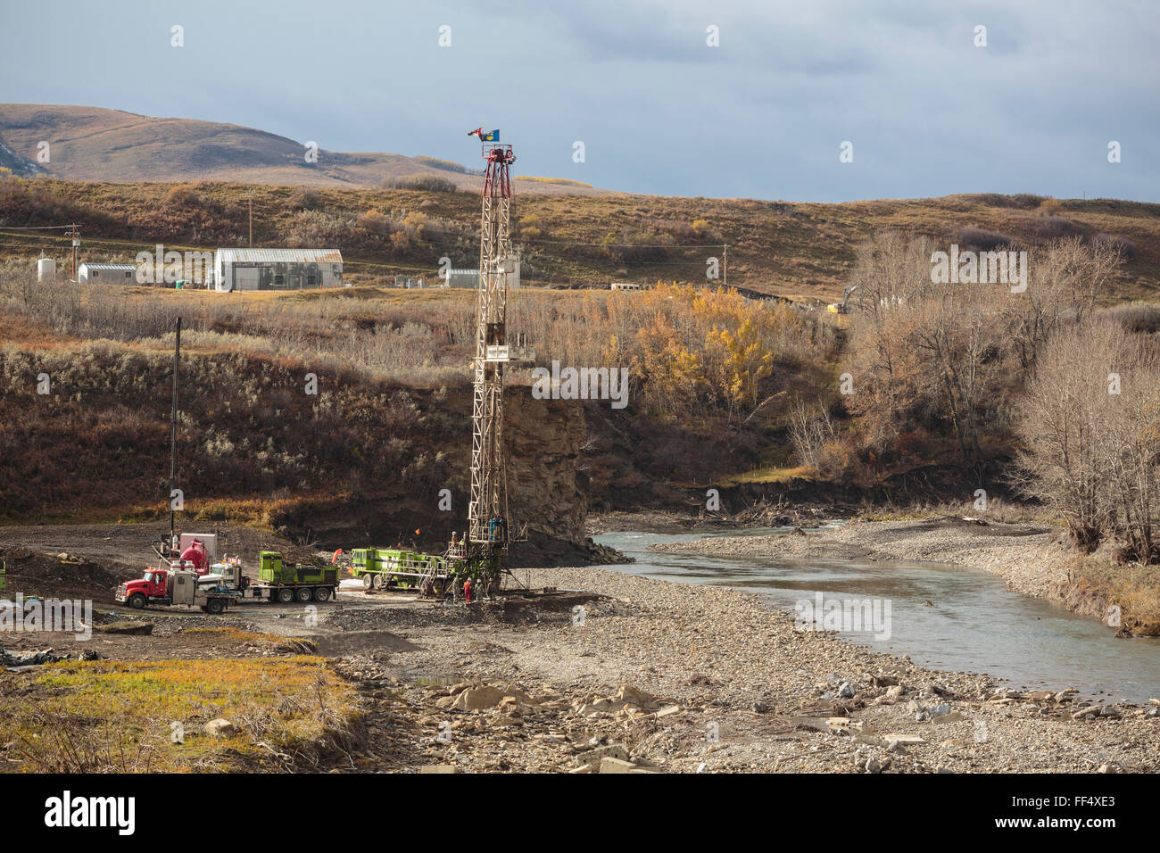 An oil and gas service rig works on a washed out wellsite along the shore of Highwood River in the southern Alberta foothills Stock Photo