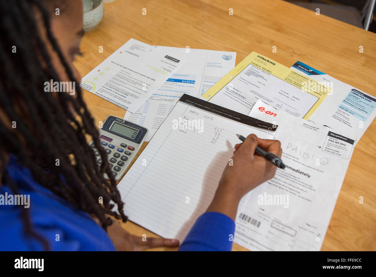 A young lady sits at her kitchen table at home checking over the household bills. Dealing with debt. Household utility bills making it difficult for a British home owner to afford. Difficulty paying gas and electricity bills is common as the economic downturn makes personal finances feel the pinch. London, UK. Stock Photo