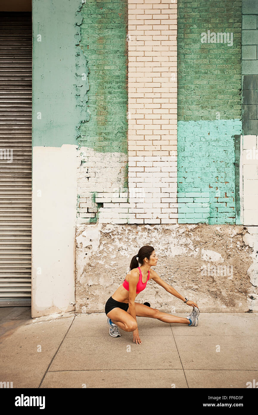 A woman in running gear, crop top and shorts, stretching her body and preparing for a run, or cooling down after exercise. Stock Photo