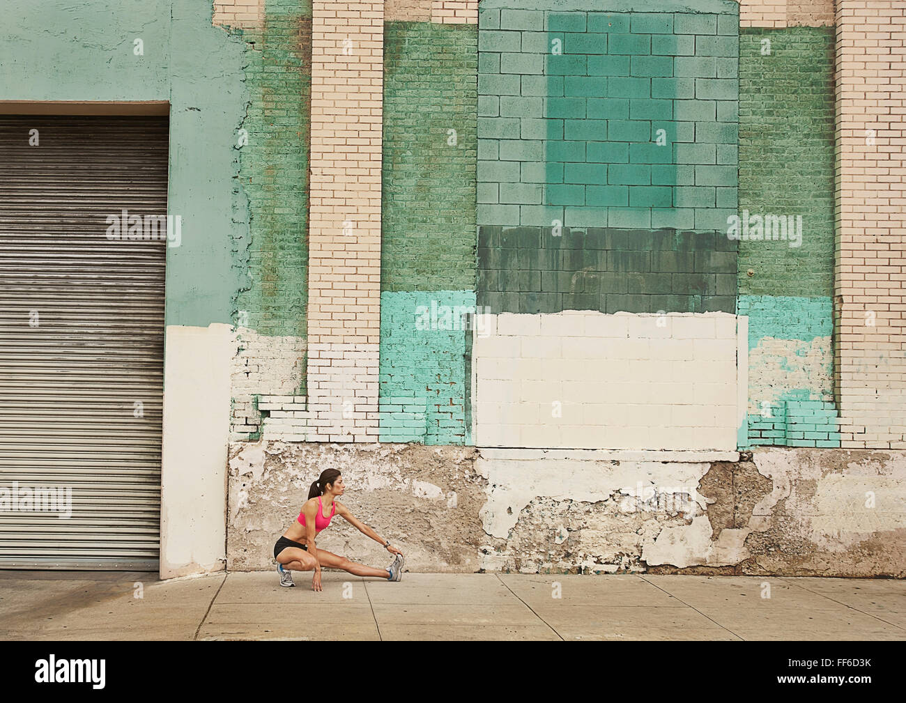 A woman in running gear, crop top and shorts, stretching her body and preparing for a run, or cooling down after exercise. Stock Photo