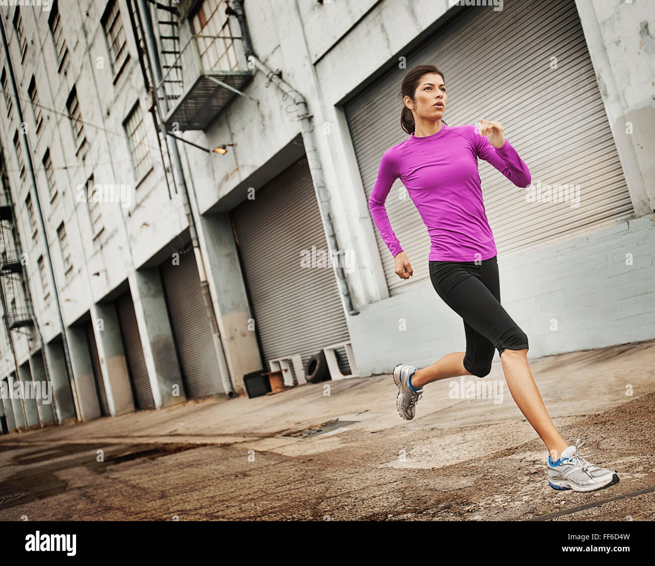 A woman running along an urban road with her arms working, stretching her legs. Stock Photo