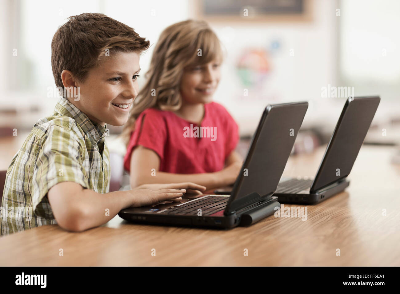 Two children seated at desks in class using laptop computers. Stock Photo