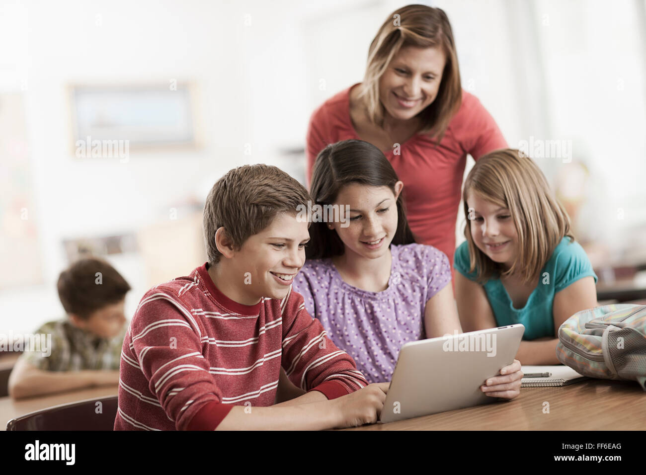 A group of students in class and an adult teacher looking at a digital tablet. Stock Photo