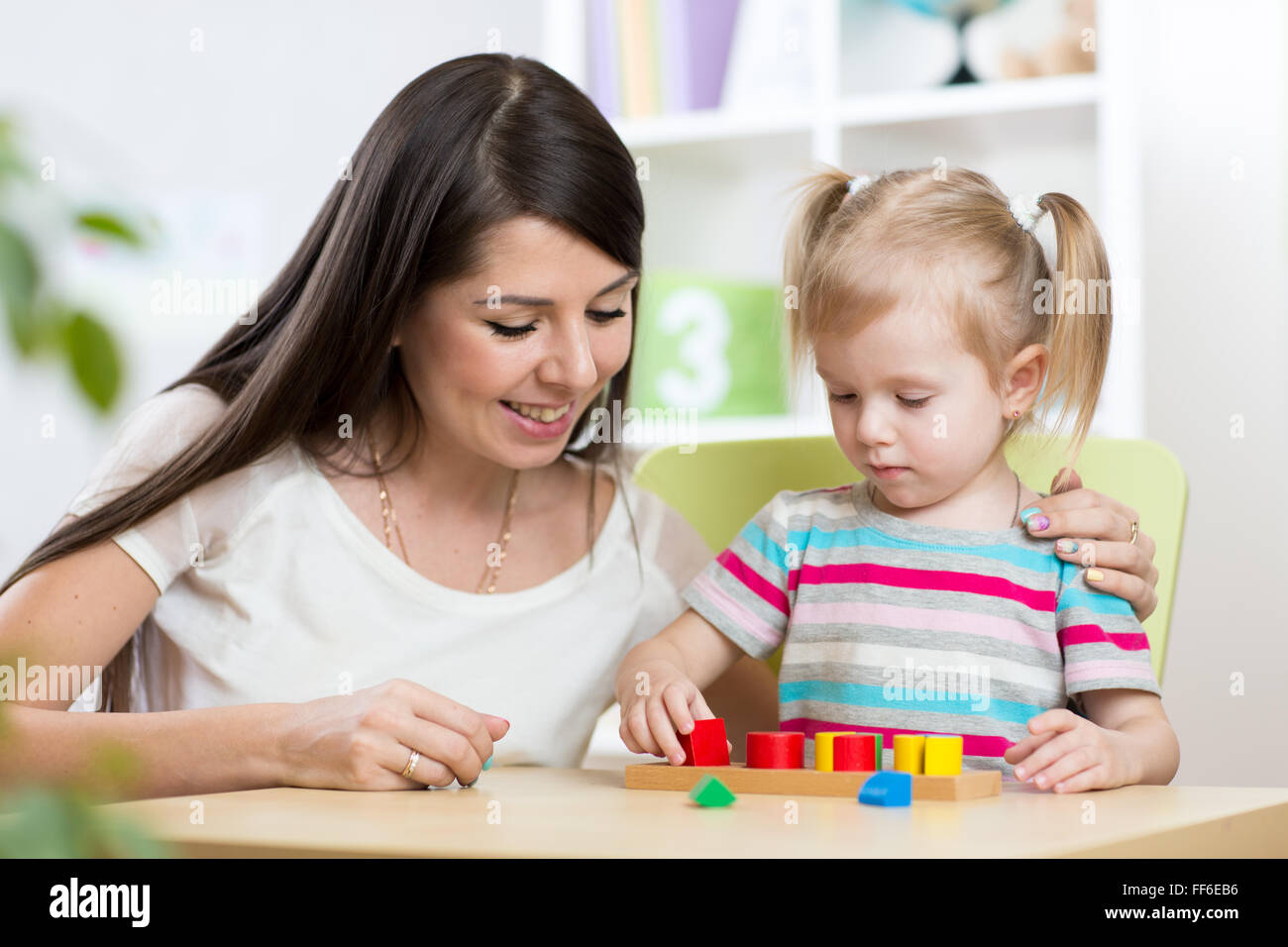 Little girl is solving puzzle. Mother watching at her actions Stock Photo