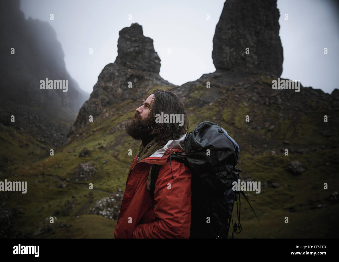 A man standing with a backdrop of rock pinnacles on the skyline towering over him, an overcast sky with low cloud. Stock Photo