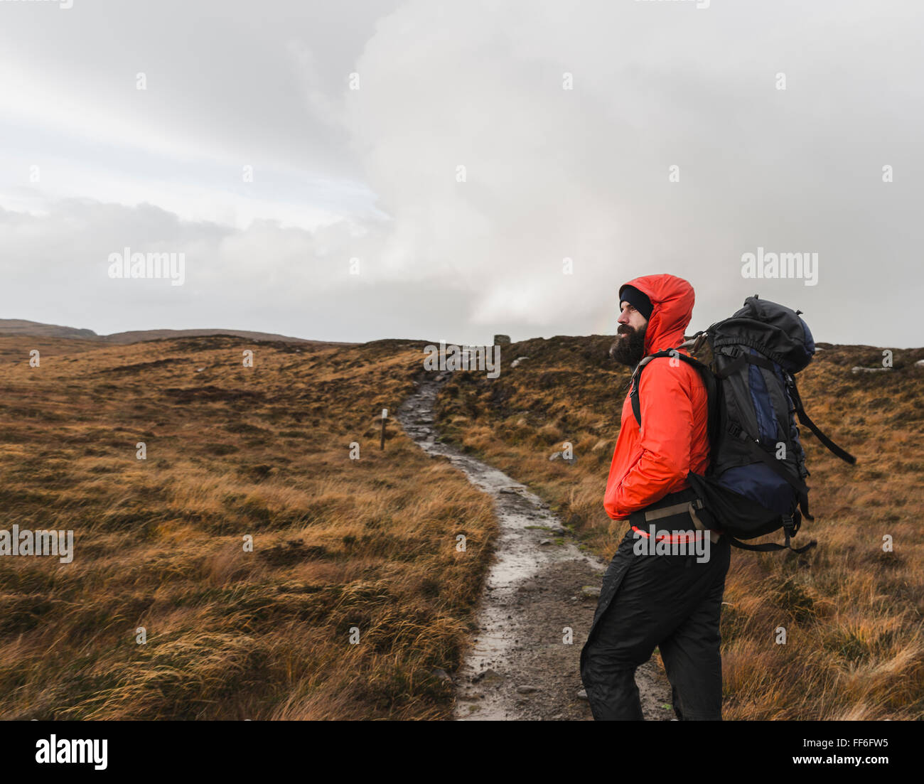 A man in winter clothing, waterproof jacket and rucksack in open countryside by a path. Stock Photo