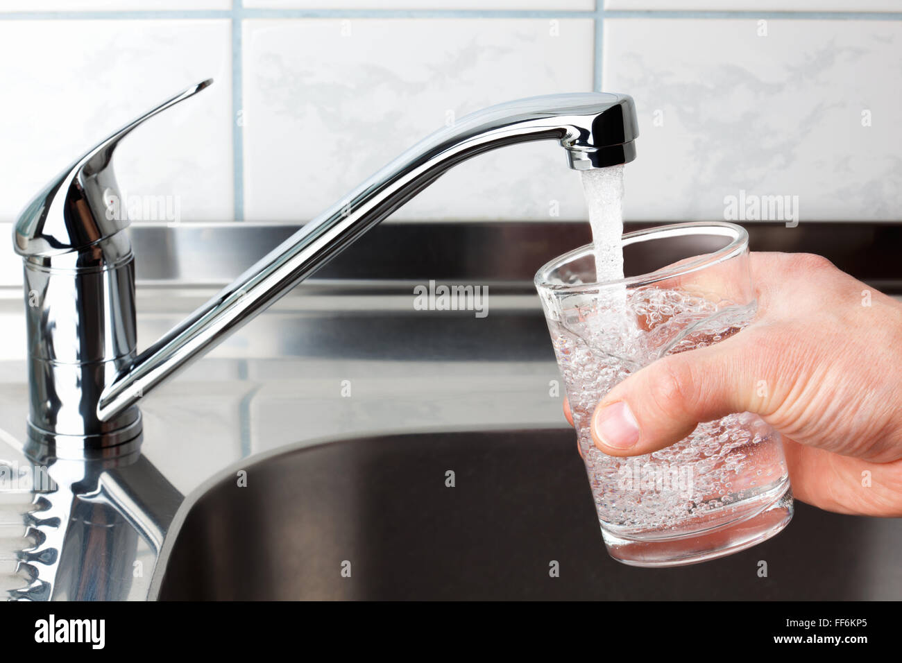 Hand holding a glass of water poured from the kitchen faucet. Stock Photo