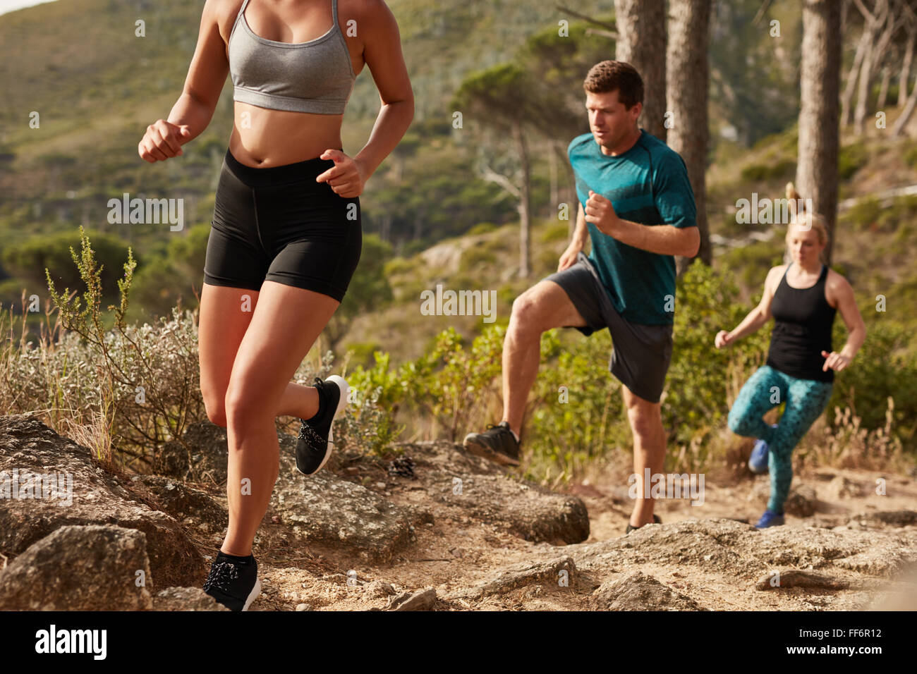 Fit young people running up a hill. Trail running training. Young and fit athletes running cross country. Stock Photo