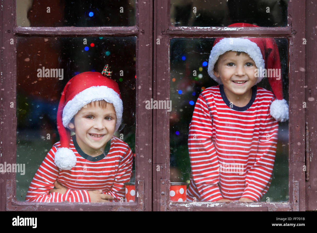 Two cute boys, brothers, looking through a window, waiting impatiently for Santa Stock Photo