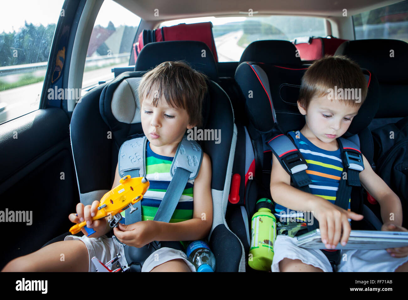 Two boy in children car seats, traveling by car and playing with toys