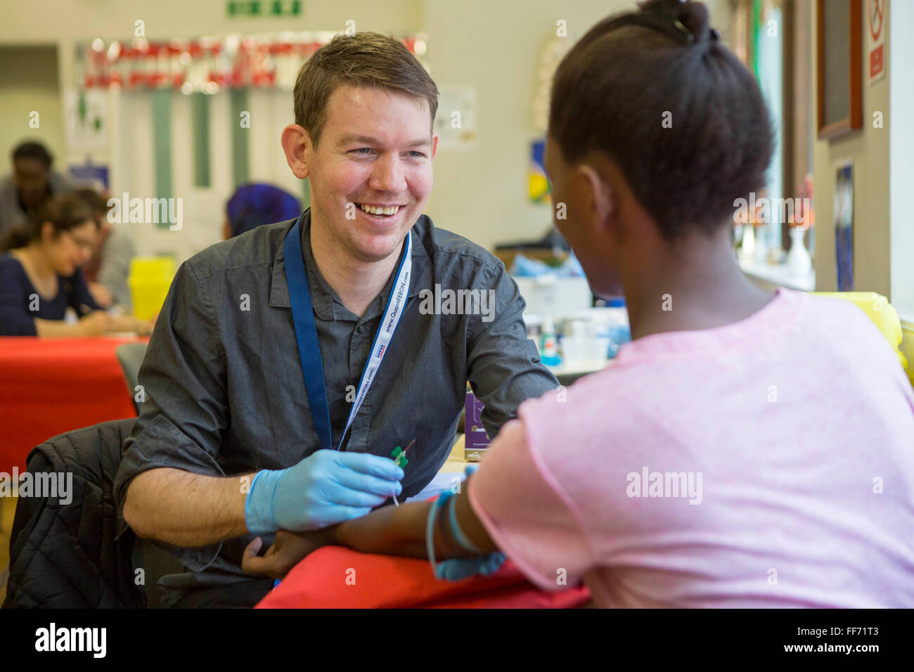 A male public health TB nurse smiles at a young female patient as her prepares her for a blood test  during a tuberculosis contact tracing screening in a hostel in central London, UK. Stock Photo
