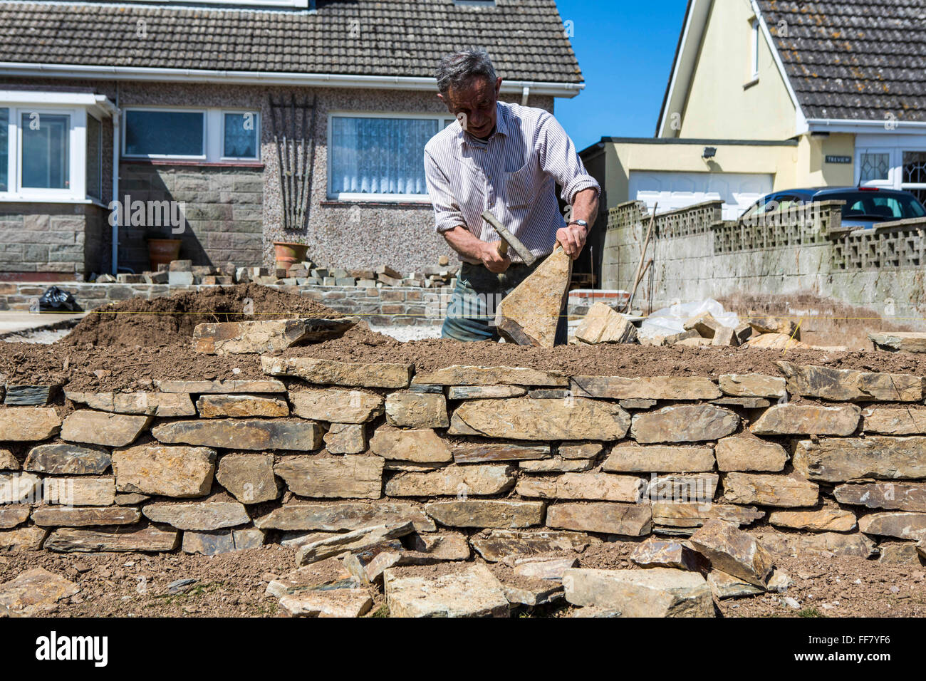 A British stonemason hammers a sandstone while constructing a wall in