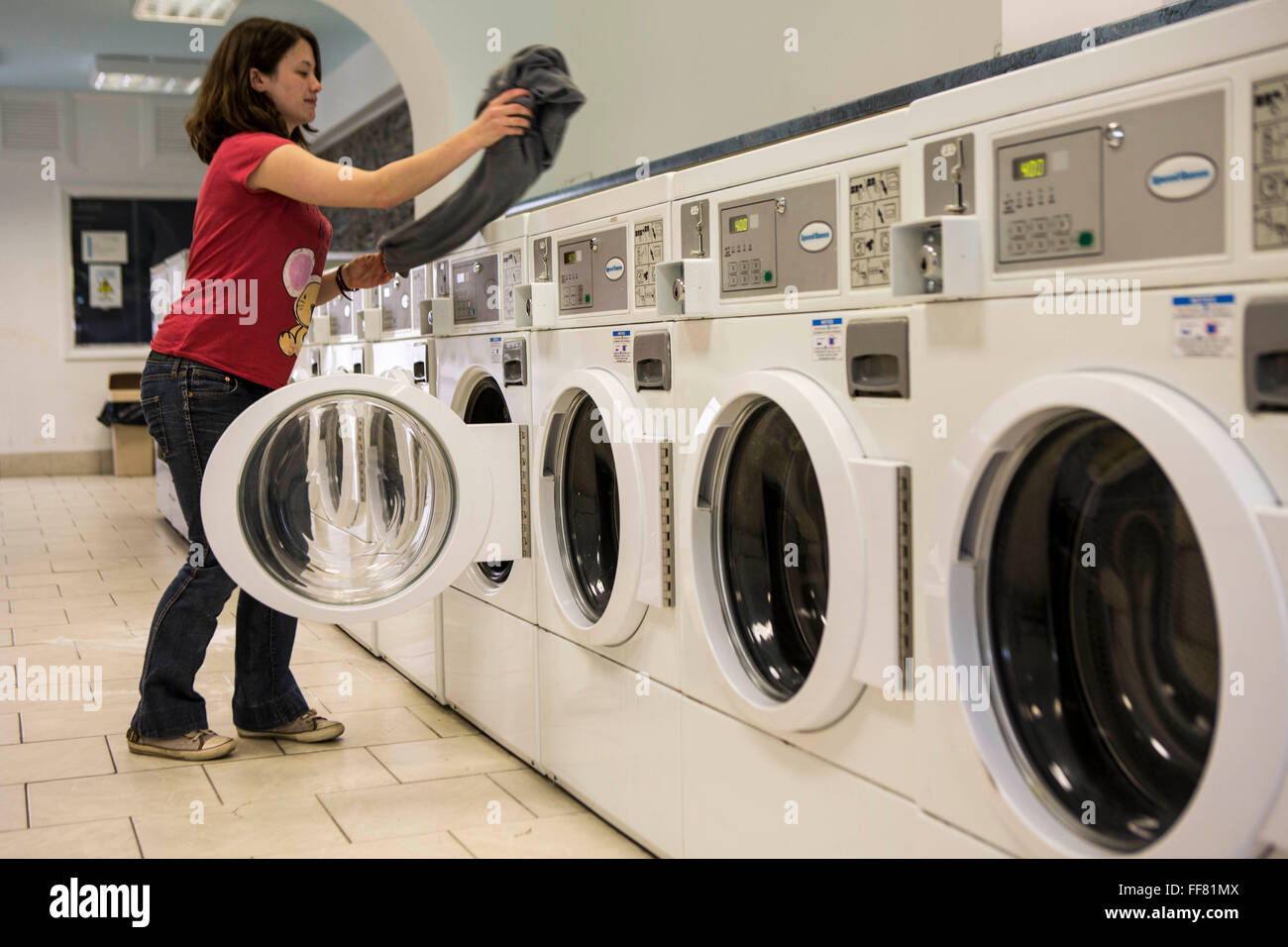 A young British woman loads clothes into a washing machine in a launderette in Wadebridge, Cornwall, UK. The energy for the launderette is sourced from roof solar panels and is part of a scheme to make this town the first to be powered by renewable sources in the UK. Stock Photo