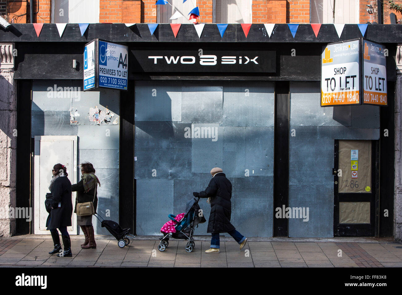 A woman with a push-chair walks past a derelict high-street shop, Lewisham, London, United Kingdom.  Many retail stores have closed down during the financial slow-down in Britain. Stock Photo