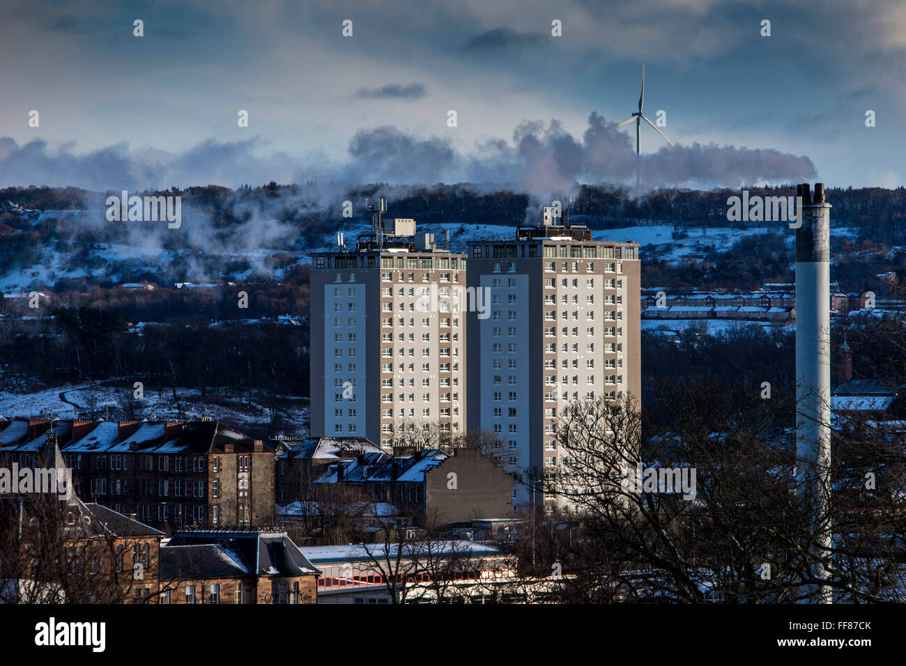 Two blocks of flats, a smoking chimney and a wind turbine on Glasgow South side taken from Queens Park, Glasgow. Stock Photo