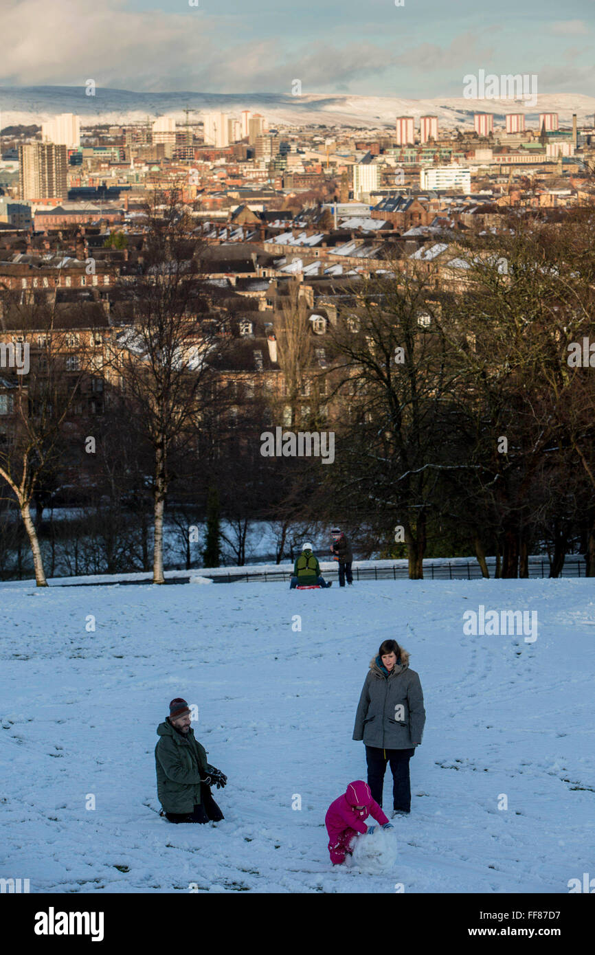 A family play in the snow, Queens Park, Glasgow.  The park is known for its view across the south side of Glasgow, with a snow covered Campsie Fells in the background. Stock Photo