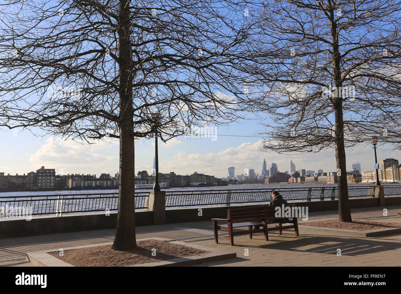 Sitting by The River Thames in the winter sun under the blue sky looking towards The City and Rotherhithe on the Thames Path Stock Photo