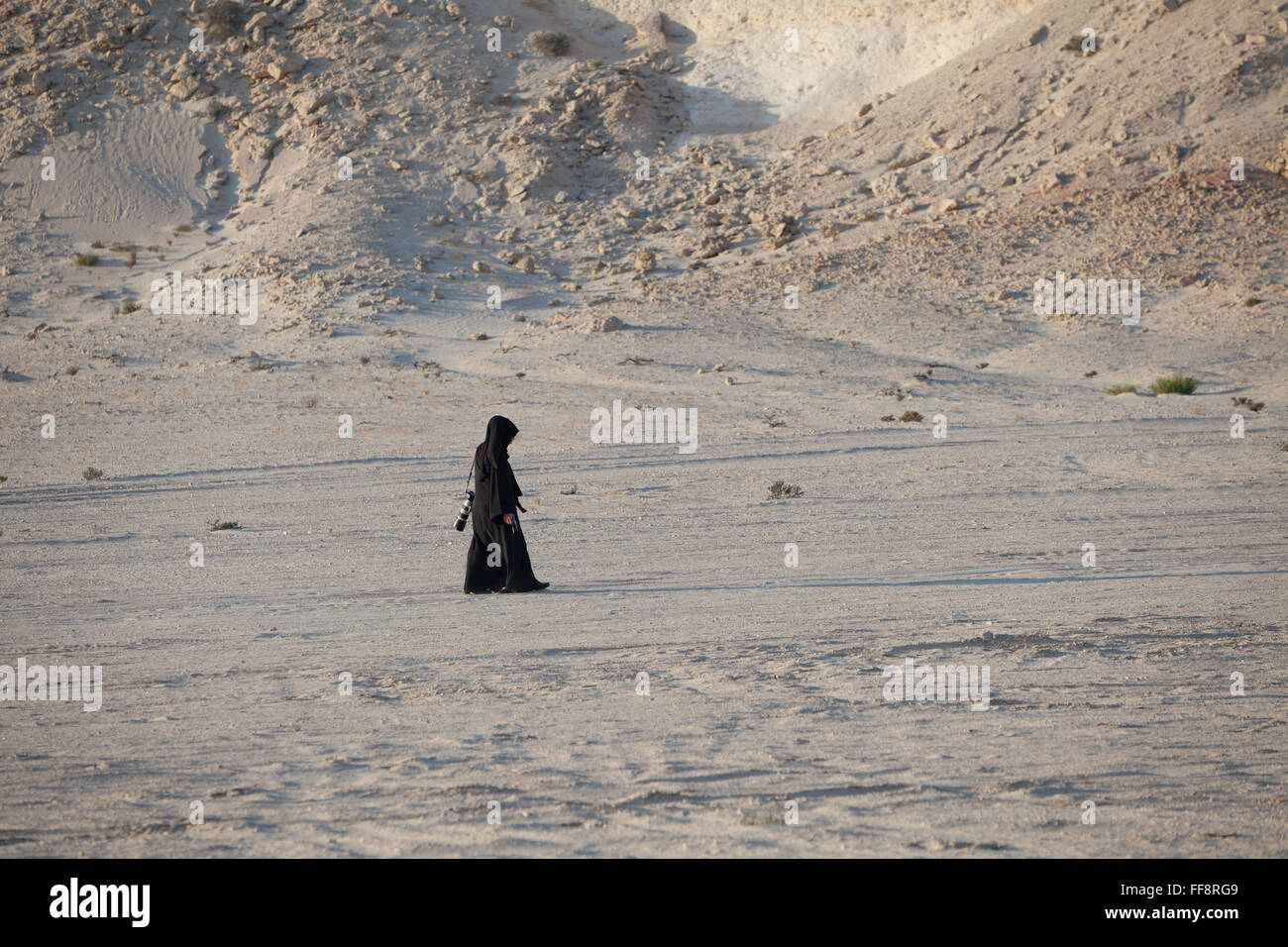 Lone Arab woman walking in Brouq Nature Reserve, Qatar desert in traditional dress, abaya, near a Gypsum plateau. Stock Photo